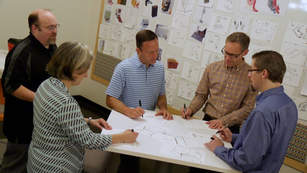 Catalyst employees stand around and criticize each other for their drawing ability.